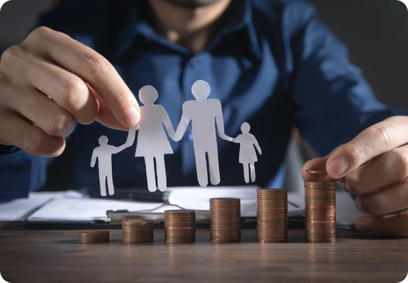 Paper cutout of a family held above stacked coins symbolizing family law costs and financial responsibility.